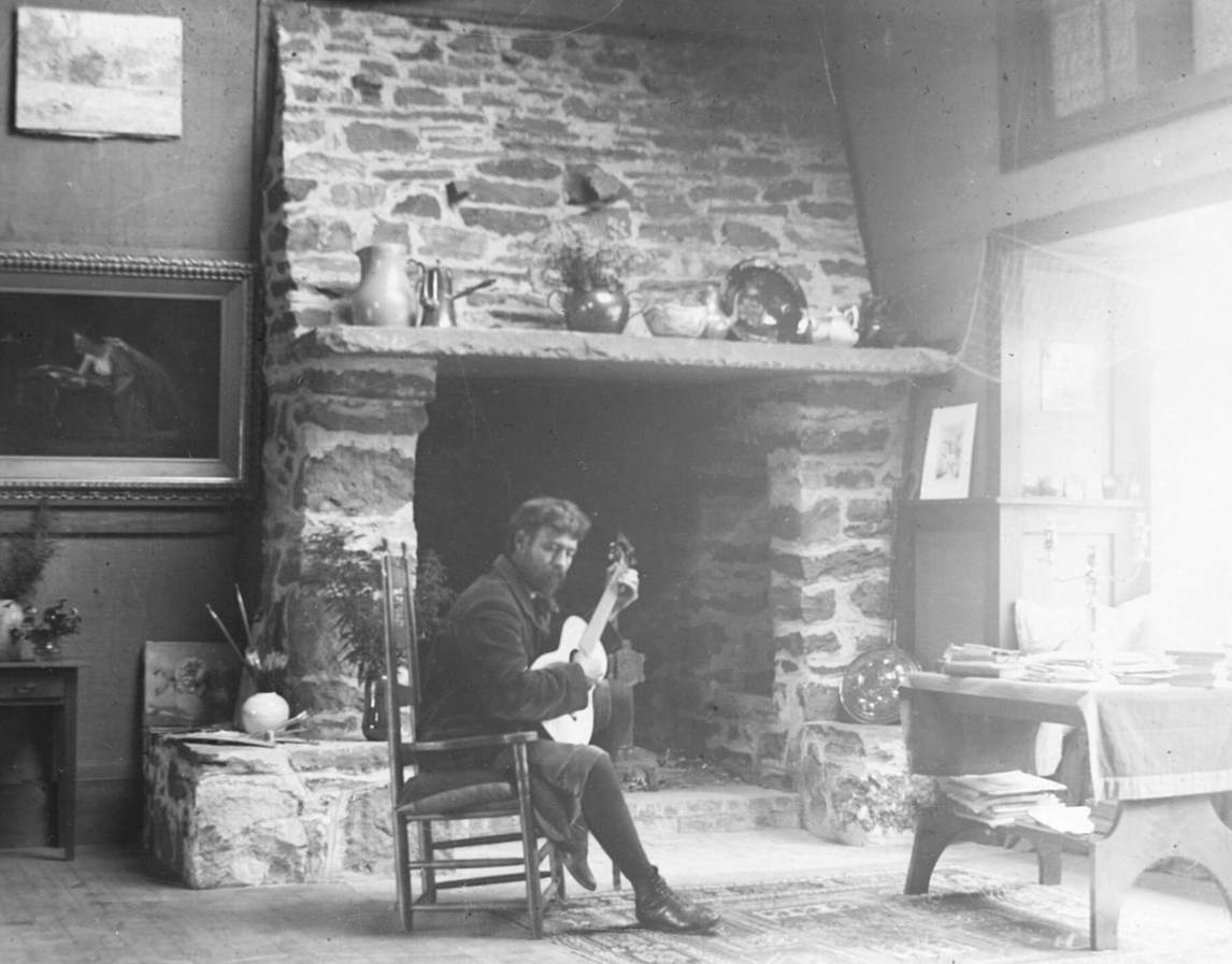 George Agnew Reid playing guitar in front of the studio fireplace, Onteora, New York, c.1893